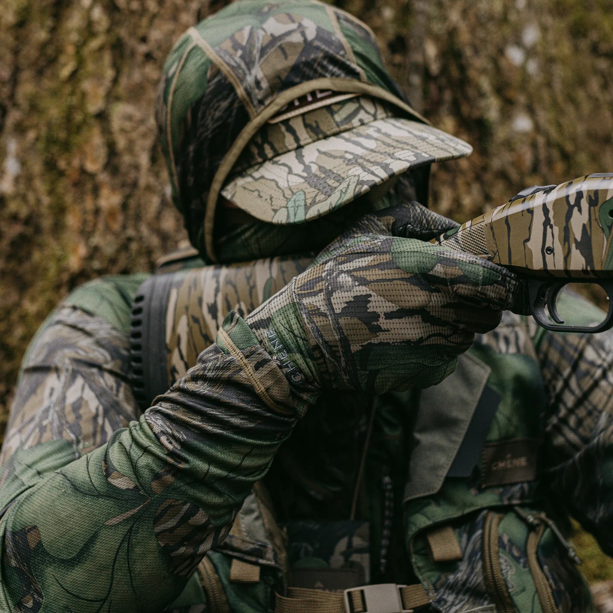 Person in full camouflage gear aiming a shotgun in a forest setting #mossy_oak_full_foliage