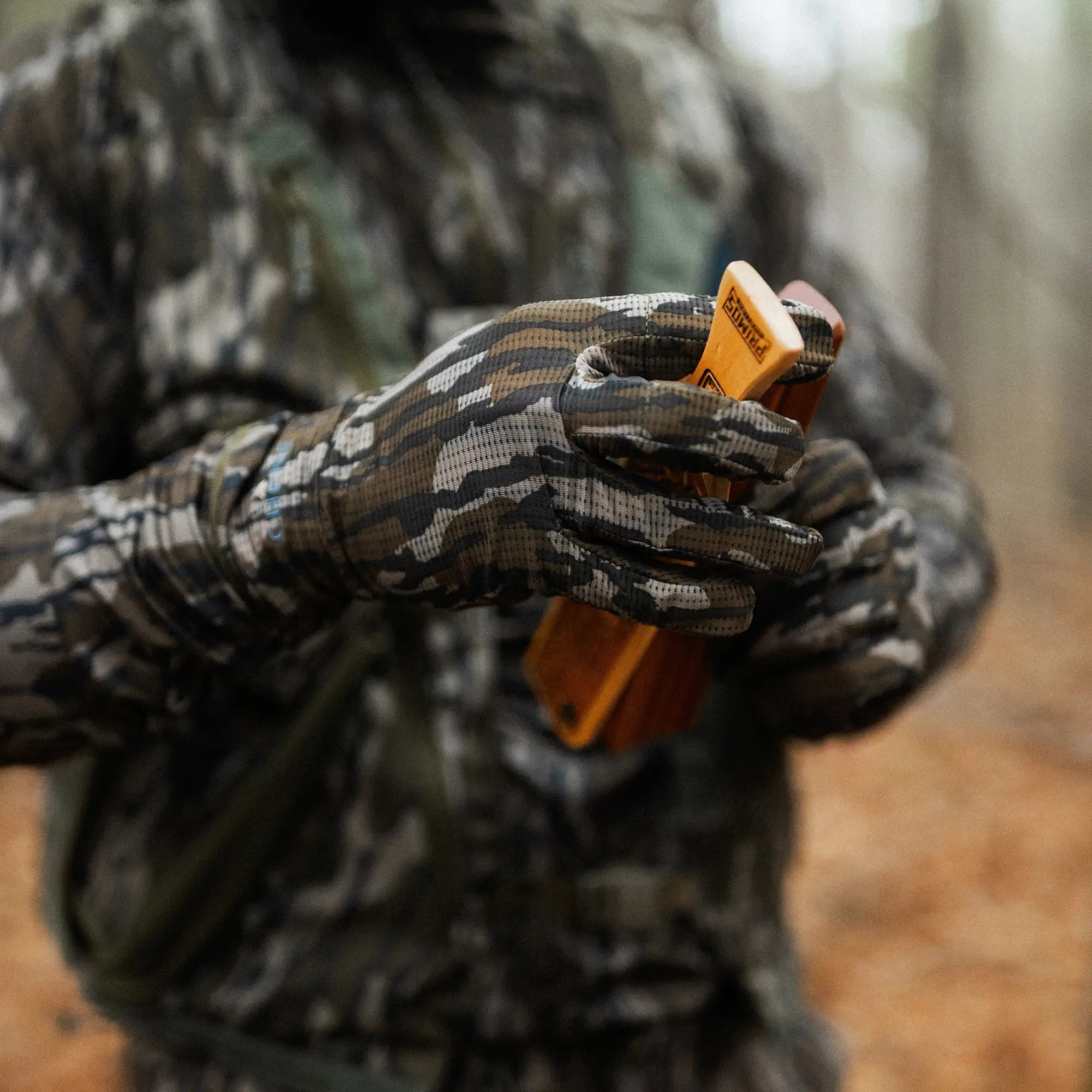 Person in camouflage clothing holding a hunting call in a forest setting #mossy_oak_original_bottomland