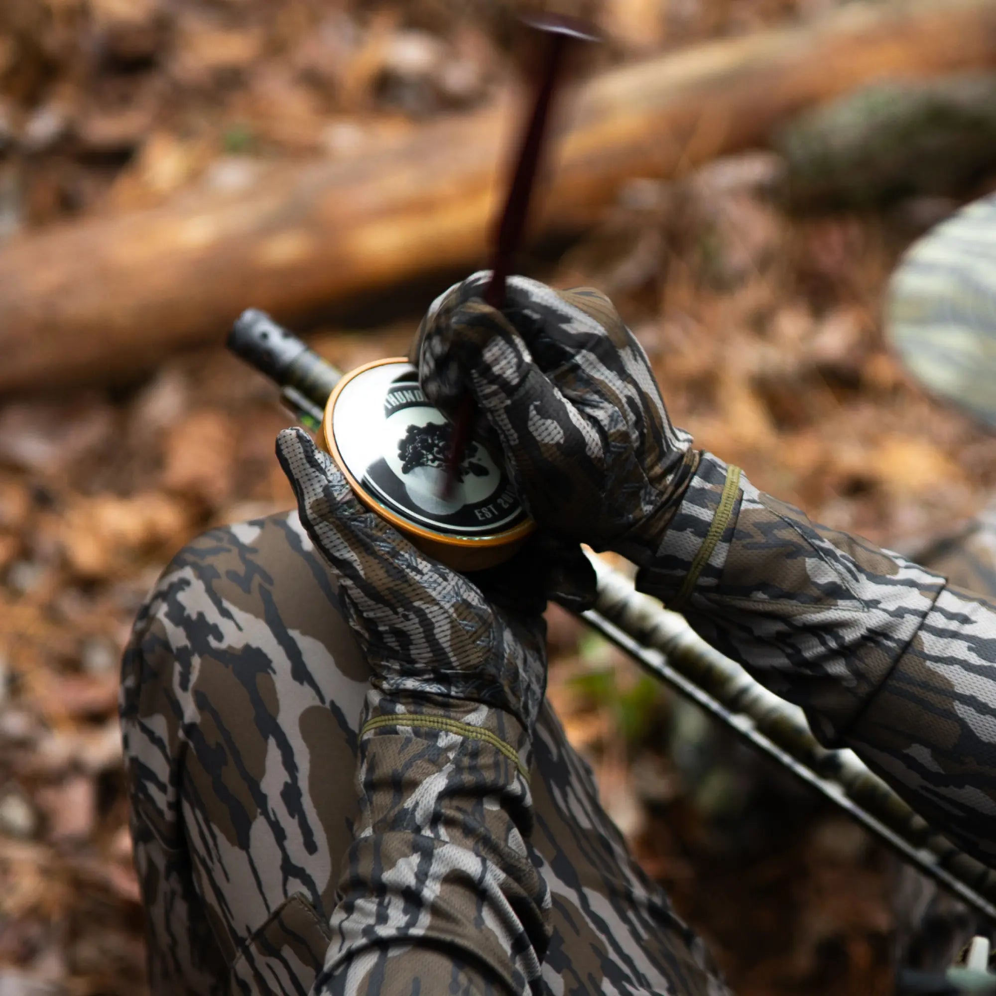 Person in camouflage gear holding a slate turkey call in a forest setting #mossy_oak_original_bottomland