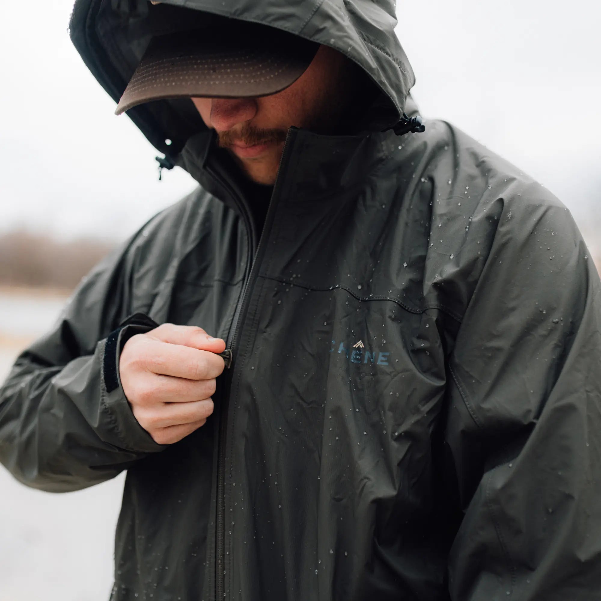 Person wearing a dark raincoat with a hood in a blurred outdoor setting #cypress