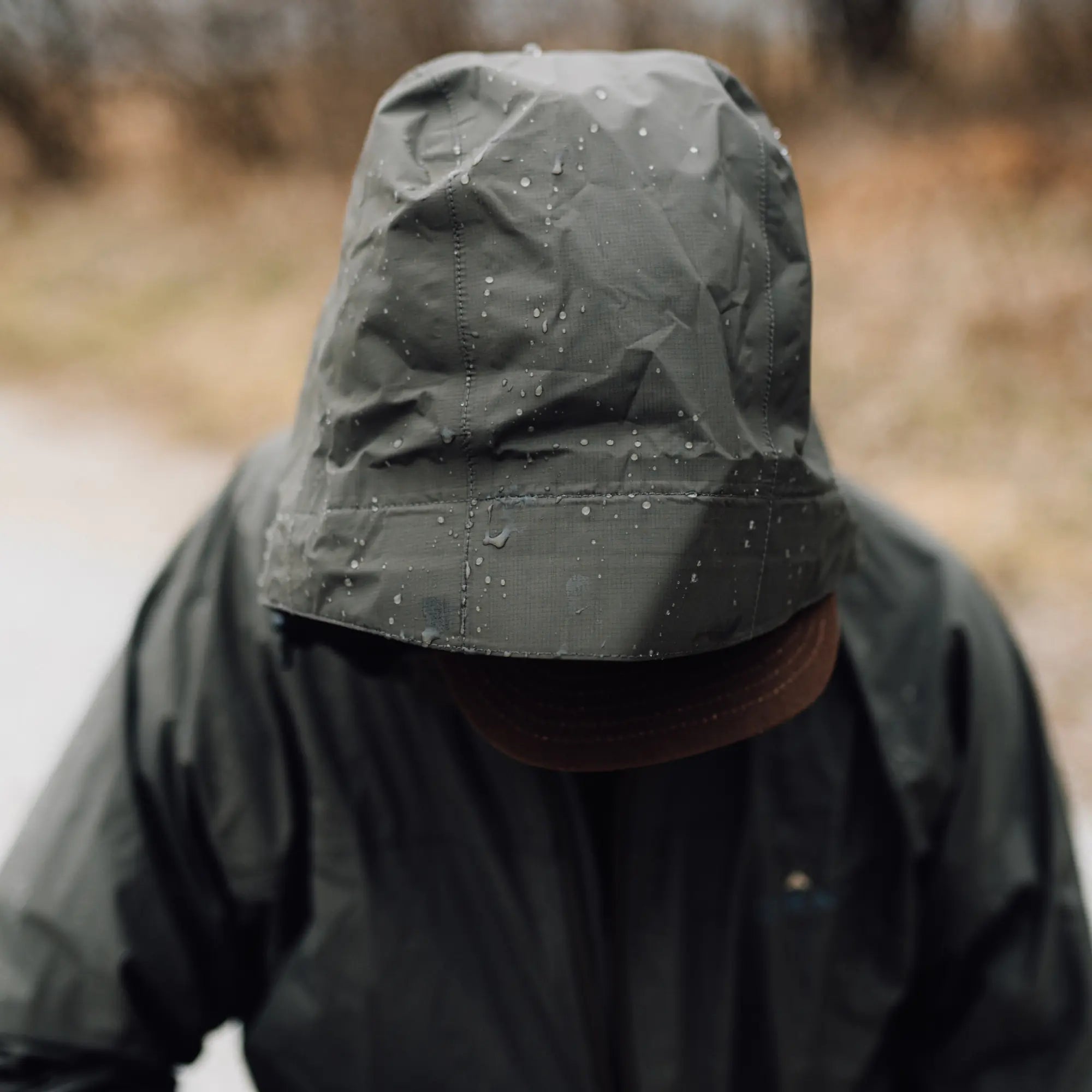 Person wearing a dark raincoat with a hood in a blurred outdoor setting #cypress